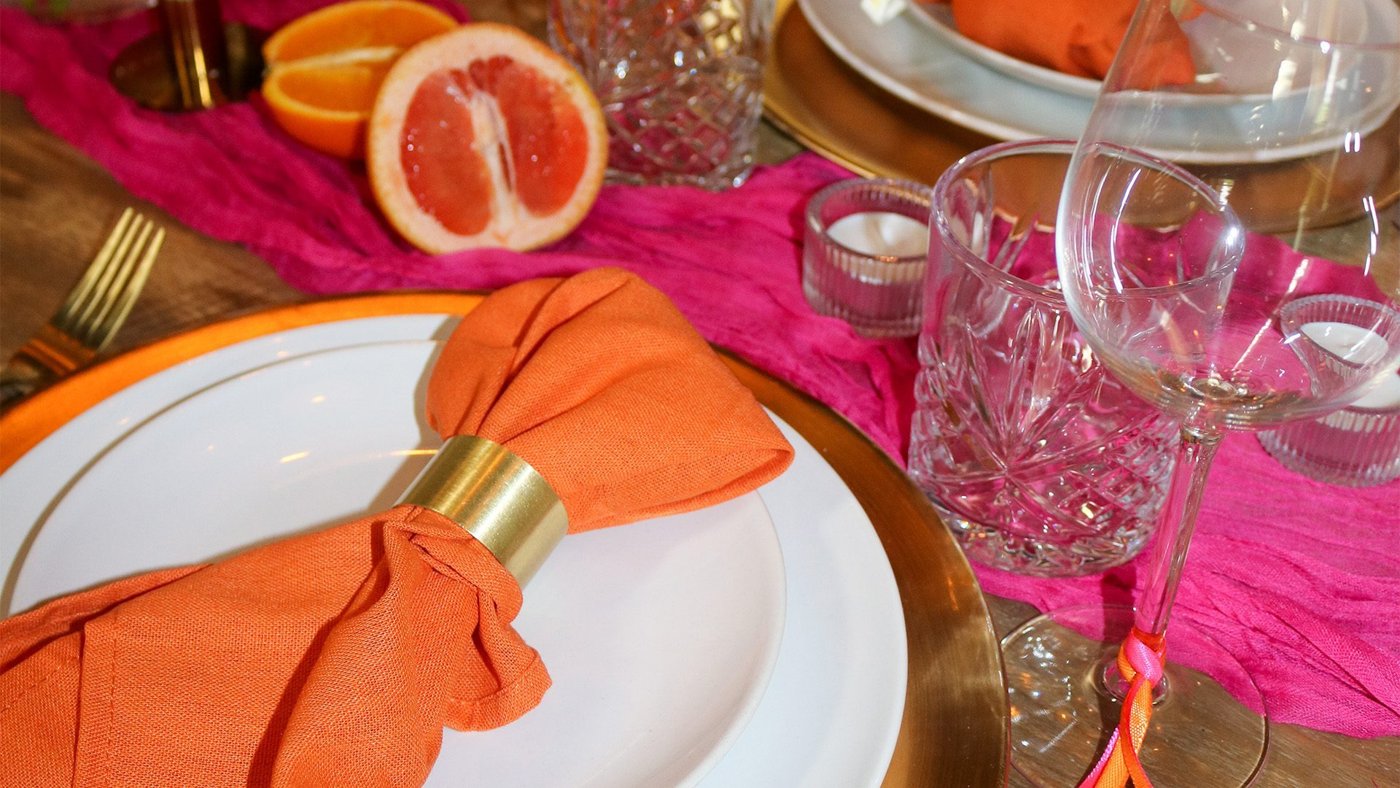 Gedekte tafel in thema Sunset met oranje servetten, gouden onderborden en fuchsia tafelloper
